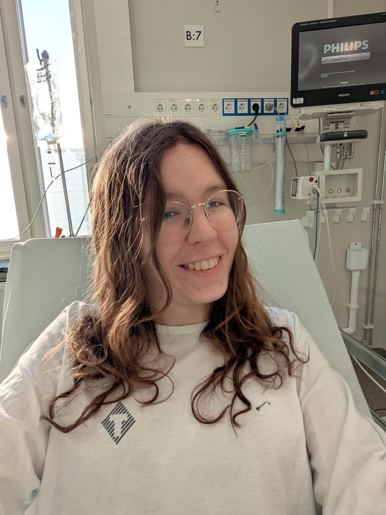 Alice in a hospital bed looking a bit drugged. She is dressed in a hospital gown and is smiling. Alice in a hospital bed looking a bit drugged. She is dressed in a hospital gown and is smiling.