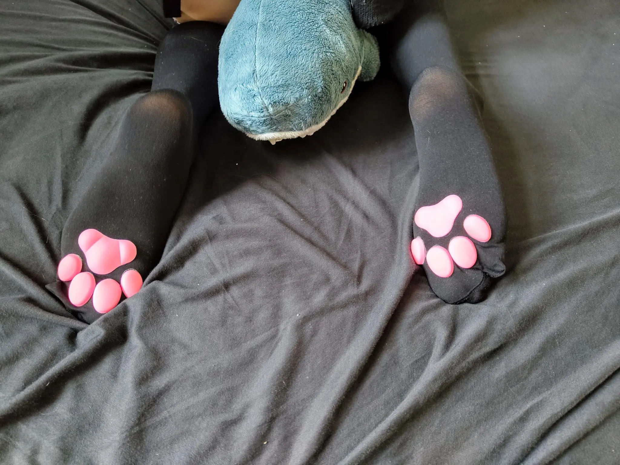 closeup of ellies feet wearing cat paw stockings on a grey bedsheet, she is sitting on a blahaj