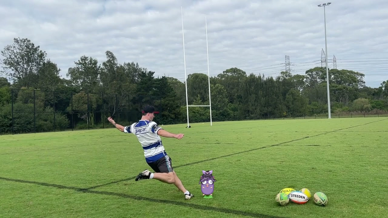 photograph taken of a rugby player on an empty rugby field, mid-running up to the rugby in an effort to kick it over the goal. however, the rugby that the player is about to kick has been replaced with lily's go mascot